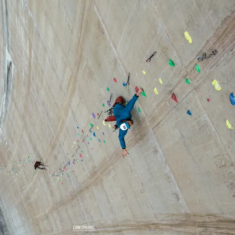 A climber on the wall of a dam, seen from above.